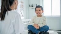 A child smiling while sitting on an exam table during a pediatric visit.