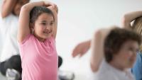 Children stretching their arms overhead during a group movement activity.