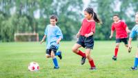 Young children chase soccer ball during game.