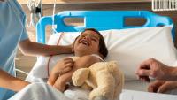 kid in a hospital bed holding teddy bear