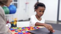 Young girl uses magnetic letter on board while therapist watches.