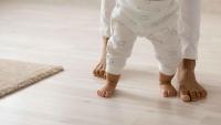 A person helping a baby take steps indoors.