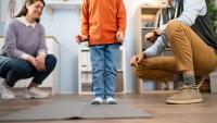 A child stands on a mat while two adults observe his leg alignment.