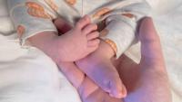 An adult hand gently supports a baby’s feet.