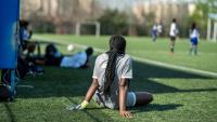 Youth athlete sitting on the sidelines of a soccer field during a game.