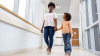 Mom walks with her kid down a hallway.