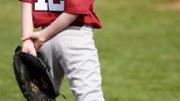 Youth baseball player standing on a field holding a glove behind their back.