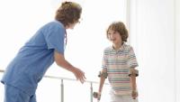 A clinician helps a young boy walking with crutches.