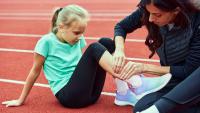 A young athlete sitting on a track while an adult examines the lower leg for pain.