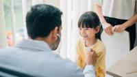 Doctor listening to a smiling child’s heartbeat during a checkup while a parent stands nearby