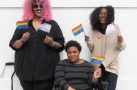 Three people holding gay and transgender pride flags