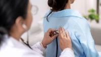 A doctor uses a stethoscope on a patient's back to listen to their lungs