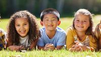 Group of five children lying on grass, smiling at the camera.