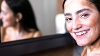 Woman with vitiligo smiling in front of a mirror.