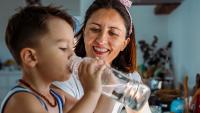 Mom helping child drink water.