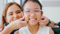 Smiling girl in a wheelchair with her mom playfully pinching her cheeks.