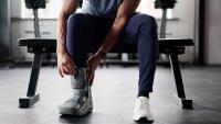 man sits on worklout bench and adjusts boot to protect ankle injury.