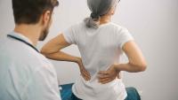 Patient holding their lower back while seated on an exam table as a clinician observes.