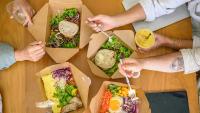 Overhead view of people eating salads together at a table.