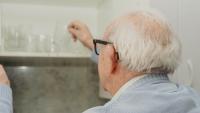 Older adult reaching into a kitchen cabinet to grab a glass.
