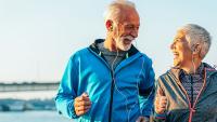 Two older adults in athletic clothing smile while exercising outdoors.