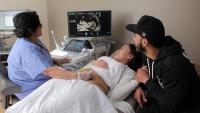 Technician doing ultrasound of expecting mother, with father watching on