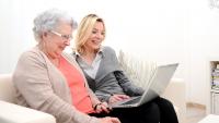 Elderly woman sits with adult daughter looking at laptop screen together