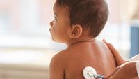 Young baby sits while being examined by doctor using stethoscope on back