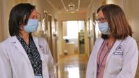 Two doctors speak to each other while standing in a hallway