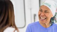 Woman undergoing treatment for cancer smiles and talks with doctor while she wears a headscarf
