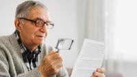 Man holds magnifying glass to read paper