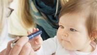 Mother holding her cute baby girl while pediatrician doing an eyesight test with diagnostic light pen