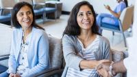 Two women sit in a waiting room, smiling. One shakes an unseen doctor's hand.