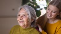 Granddaughter combing grandmother's hair in bedroom at home.