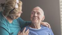 Edlerly man smiles at wife and caretaker.
