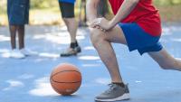 Senior man stretches his knee and hips while warming up to play basketball.