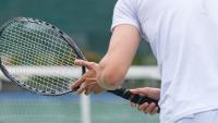 Man holds tennis racquet facing net.