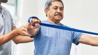 Patient exercising with a resistance band during a rehabilitation session with his physiotherapist