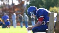 football player in pads and equipment on the bench with head hanging