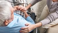 Elderly man in wheelchair comforted by his caregiver