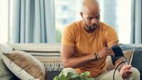 man sitting on sofa and measuring his blood pressure