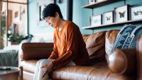 older asian woman sitting on couch in pain