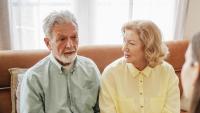 Elderly patient answers question from doctor while spouse looks on.