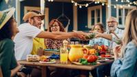 A family sits at a picnic table and shares a meal at a summer cookout.
