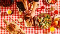 Food spread out on a picnic tablecloth during a summer cookout.