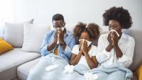 family sitting together on a couch blowing their noses because they are sick