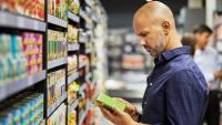 Man in blue shirt looks at box of food in grocery store.
