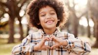 Smiling child making a heart shape with hands.