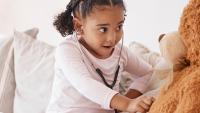 Young girl using a stethoscope to play doctor with a teddy bear.