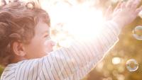 Young child reaching for bubbles.